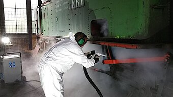 Industrial use of dry ice blasting to clean a machine without water: Employees wearing protective gear remove contaminants gently and without leaving residue using a CO₂ cleaning system