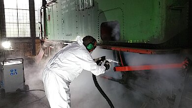 Industrial use of dry ice blasting to clean a machine without water: Employees wearing protective gear remove contaminants gently and without leaving residue using a CO₂ cleaning system