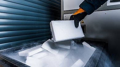 Gloved hand holds a dry ice block over a container with CO₂ vapour