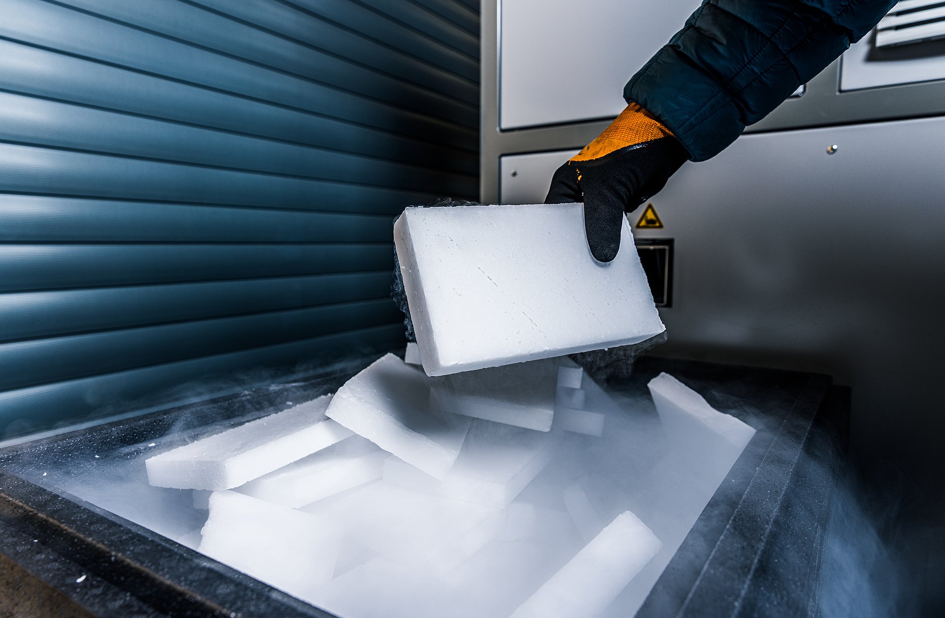 Gloved hand holds a dry ice block over a container with CO₂ vapour