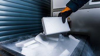 Gloved hand holds a dry ice block over a container with CO₂ vapour