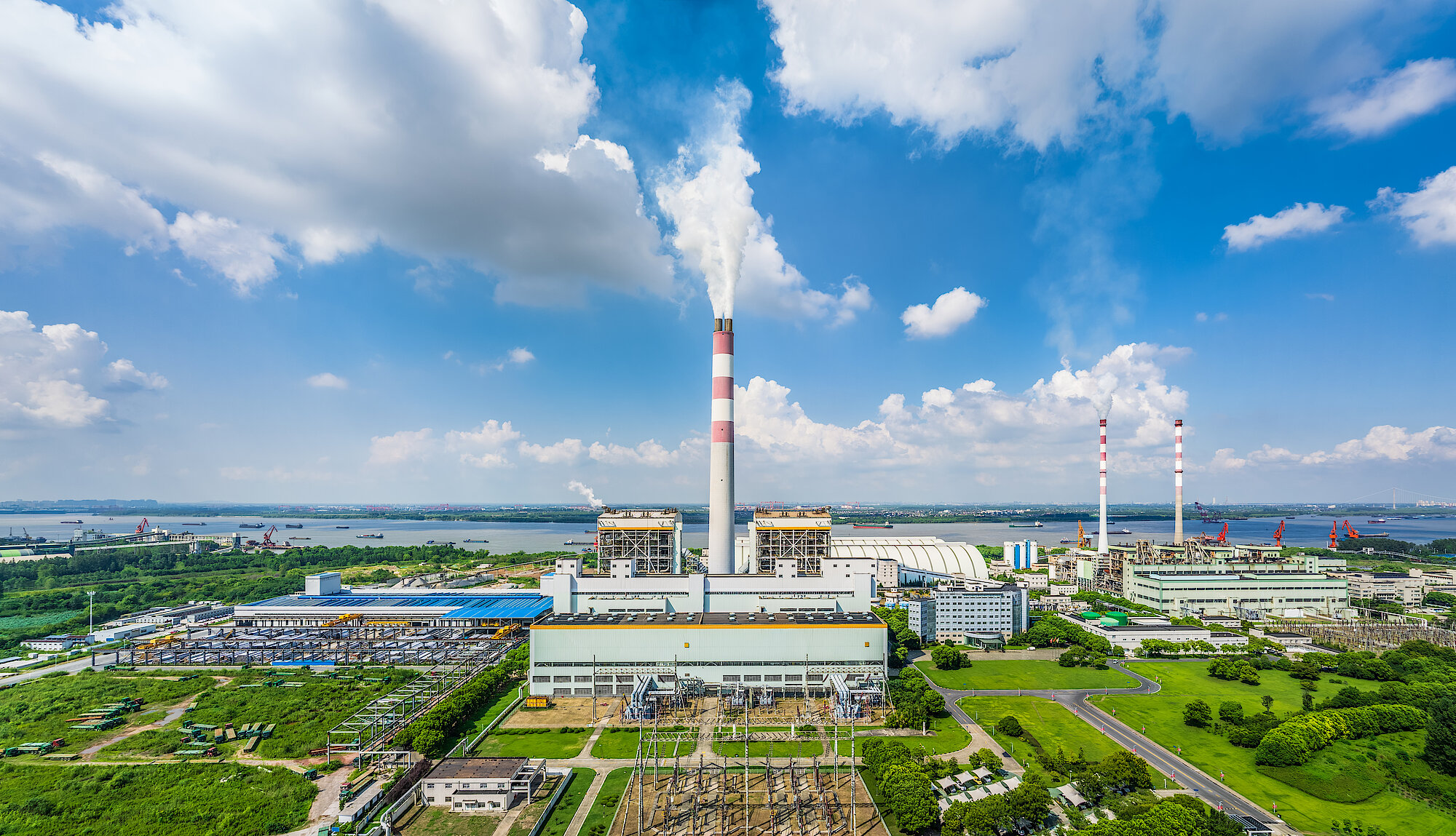 Industrielle Anlage mit Schornstein und aufsteigendem Rauch in grüner Umgebung – Symbolbild für CO2-Rauchgas-Rückgewinnung.
